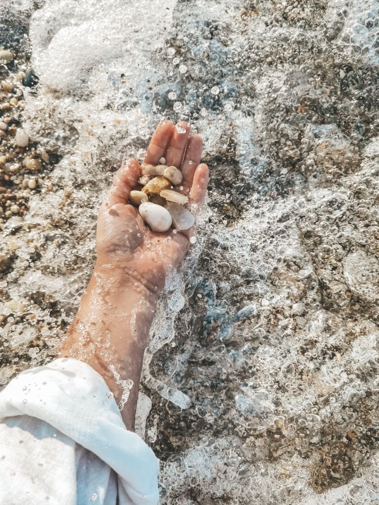 كفّ تمسك حصى مبللة بينما تغسلها مياه البحر الرغوية على الشاطئ